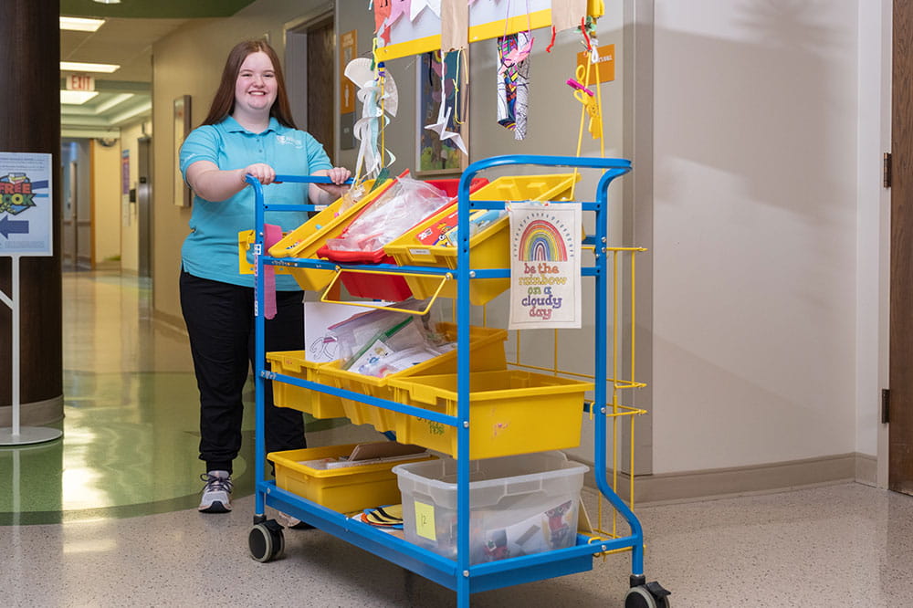 Foto de un voluntario de Arkansas Children's empujando un carrito de actividades.