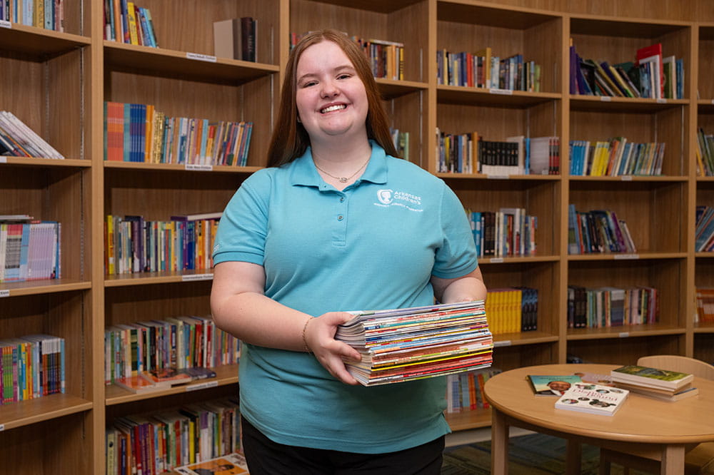 Foto de un voluntario de Arkansas Children's sosteniendo libros en la biblioteca.