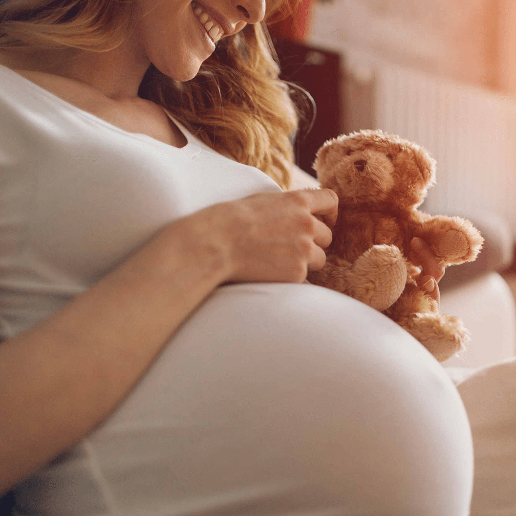 Image of pregnant woman with teddy bear on belly.
